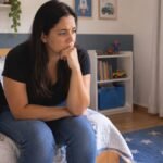 Mãe preocupada ao lado da mochila pronta que o filho não quer levar